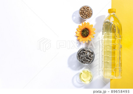 Flat lay composition of bowls of sunflower seeds and sunflower oil on white and yellow background with copyspace. 89658493