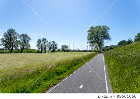 A neatly 2 lane asphalted cycle path along the A44 and the meadows towards Sassenheim train Station in the South-Holland municipality of Teylingen on a sunny day in the Netherlands. 89661066