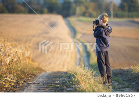 Young child boy with photo camera taking picture of wheat field on blurred rural background. Young child boy with photo camera taking picture of wheat field on blurred rural background. 89661857