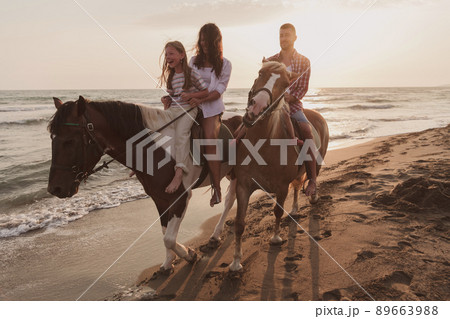 The family spends time with their children while riding horses together on a sandy beach. Selective focus  89663988