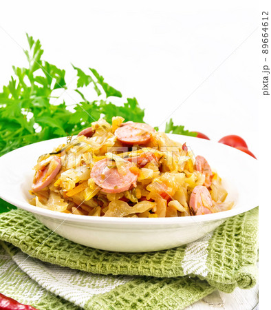 Cabbage stew with sausages in white plate on wooden board 89664612