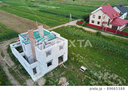 Aerial view of unfinished frame of private house with aerated lightweight concrete walls and wooden roof beams under construction. Aerial view of unfinished frame of private house with aerated lightweight concrete walls and wooden roof beams under construction. 89665388