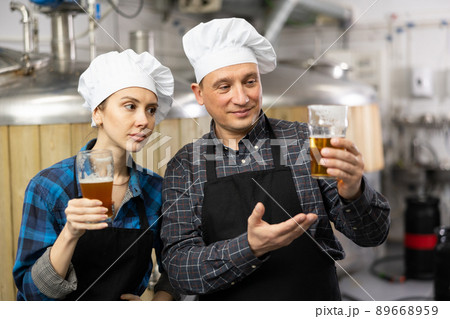 Woman and man brewmasters checking quality of beer and discussing Woman and man brewmasters checking quality of beer and discussing 89668959
