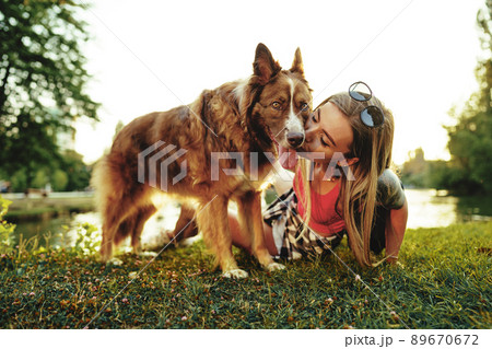 Close up portrait of young woman kissing her dog in the park 89670672