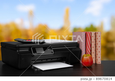Compact home printer on desk with books against blurred background Compact home printer on desk with books against blurred background 89670814