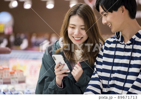 スーパーでスマホを見て買い物をする若い男女 89671713