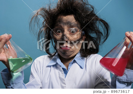 Confused silly chemistry expert holding glass jars filled with toxic chemical liquid substances while looking at camera. Puzzled crazy chemist having beakers filled with blood samples. Studio shot. 89673617
