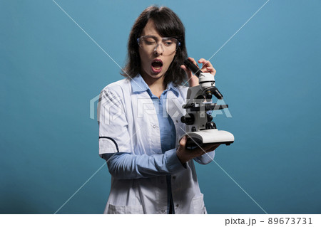 Microbiology expert with shock expression analyzing scientific discovery using modern microscope. Amazed researcher investigating bacteria experiment results while using magnifying instrument. Microbiology expert with shock expression analyzing scientific discovery using modern microscope. Amazed researcher investigating bacteria experiment results while using magnifying instrument. 89673731