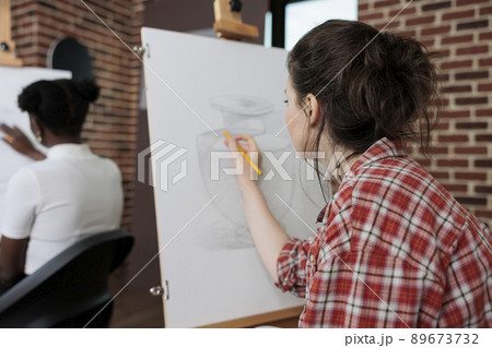 Painter woman drawing artistic vase on white canvas working at illustration technique using graphic pencil during art lesson in creativity studio. Multiethnic team developing creative skill Painter woman drawing artistic vase on white canvas working at illustration technique using graphic pencil during art lesson in creativity studio. Multiethnic team developing creative skill 89673732
