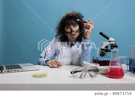 Mad looking foolish biochemist holding glass test tubes filled with unknown experimental liquid substance while looking at camera. Crazy scientist with wild look having tubes filled with blood samples 89673759