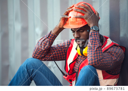 African American male technician or engineer. Sit near a container and look tired and sleepy or unemployed. Logistics industrial cargo mover concept. 89673781