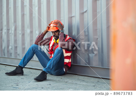 African American male technician or engineer. Sit near a container and look tired and sleepy or unemployed. Logistics industrial cargo mover concept. 89673783
