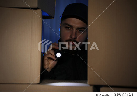 Security guard with flashlight looking through pile of cardboard boxes in dark room 89677712