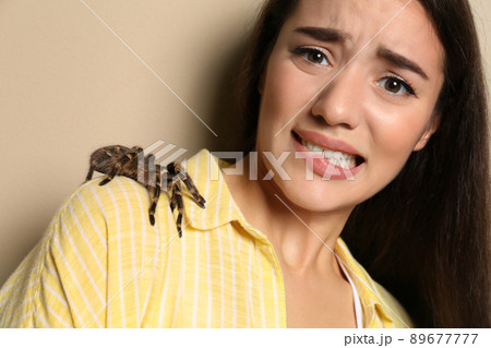 Scared young woman with tarantula on beige background. Arachnophobia (fear of spiders) Scared young woman with tarantula on beige background. Arachnophobia (fear of spiders) 89677777
