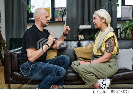 Side view of handsome mature man telling something to his tattooed girlfriend using sign language Side view of handsome mature man telling something to his tattooed girlfriend using sign language 89677835