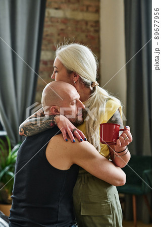 Vertical medium shot of tattooed mature woman holding cup of coffee embracing her loving boyfriend 89677956