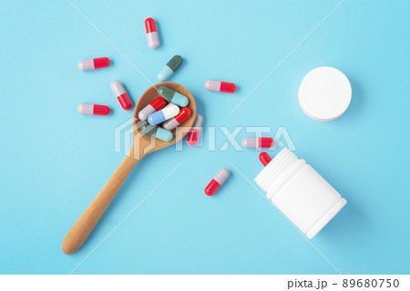 Pills on wooden spoon with white medicine bottle on blue background 89680750