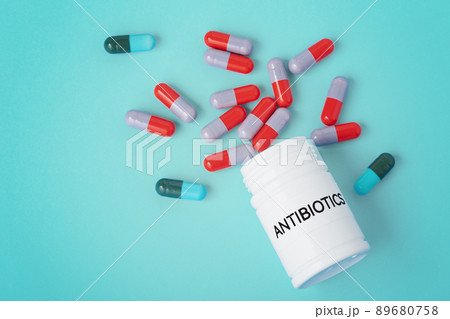 Antibiotic concept, heap of capsule pills spilled out from medicine bottle on green background 89680758