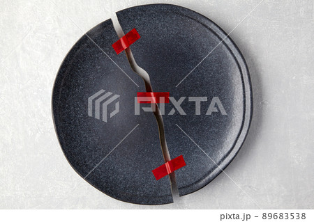 Broken plate is taped together on a light gray concrete table Broken plate is taped together on a light gray concrete table 89683538