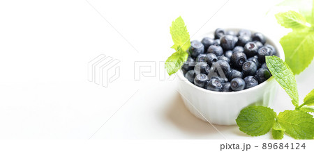 Advertising banner for natural healthy food. White bowl with forest blueberries and fresh green mint leaves on white. Blueberry - natural superfood. Close up. Copy space for text or design. 89684124