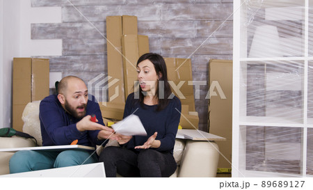 Girlfriend hitting boyfriend with instructions while assembling furniture in their new apartment. Girlfriend hitting boyfriend with instructions while assembling furniture in their new apartment. 89689127