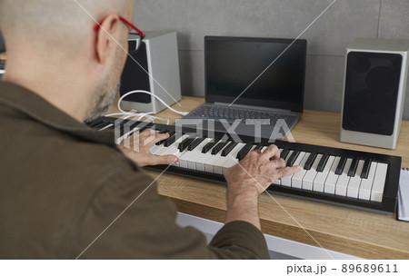 Man is rehearsing while playing on compact modern synthesizer in his home music studio. 89689611