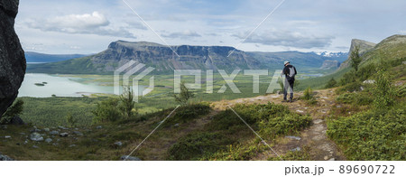 Panoramic scenic view of glacial Rapadalen river delta valley with lonely hiker figure, Skierffe rock summit at Sarek national park, meanders, lakes, blue mountains, forest. Summer landscape Sweden Panoramic scenic view of glacial Rapadalen river delta valley with lonely hiker figure, Skierffe rock summit at Sarek national park, meanders, lakes, blue mountains, forest. Summer landscape Sweden 89690722