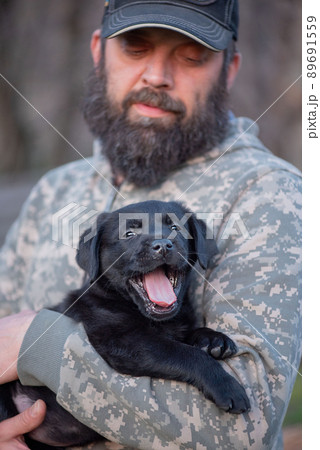 Man in military clothes with a Labrador Retriever puppy in his arms. Man and dog. Man in military clothes with a Labrador Retriever puppy in his arms. Man and dog. 89691559