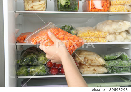 Woman putting plastic bag with carrot in refrigerator with frozen vegetables, closeup 89693293