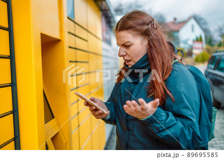 Caucasian angry woman with smartphone app at outdoor automated parcel machine. Mail delivery and post service concept Caucasian angry woman with smartphone app at outdoor automated parcel machine. Mail delivery and post service concept 89695585