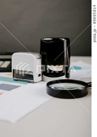 Office desktop with documentsm magnifier and stamp close-up. Vertical image 89695814