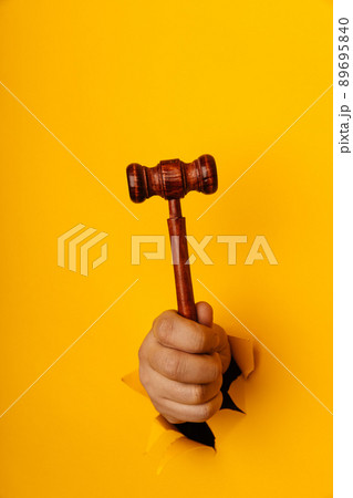 Male hand holding a wooden gavel through torn yellow background. Law and auction aconcept. Vertical image Male hand holding a wooden gavel through torn yellow background. Law and auction aconcept. Vertical image 89695840