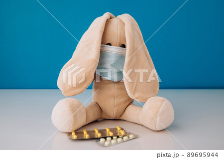 Bunny toy in mask with pills on a blue background. Children's illnesses concept 89695944