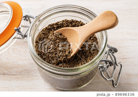 Whole dill seeds and wooden spoon in a clip top glass jar close-up. 89696336