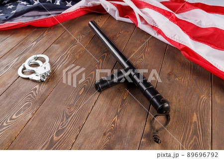 silver metal handcuffs and police nightstick near US flag on wooden surface 89696792