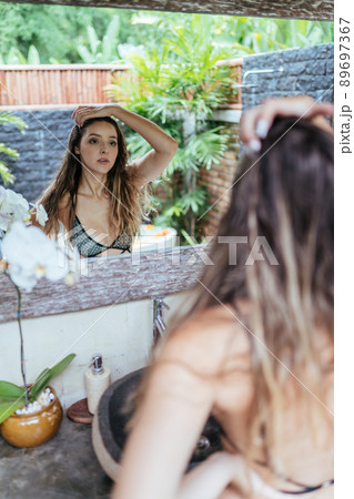 very carefully examines in the mirror her face beautiful girl in a swimsuit very carefully examines in the mirror her face beautiful girl in a swimsuit 89697367