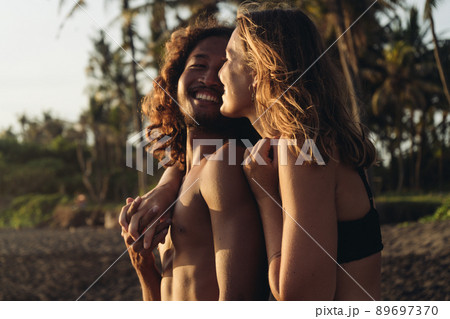 A loving couple against a background of palm trees and sand stand in a hug and smile at each other man and woman A loving couple against a background of palm trees and sand stand in a hug and smile at each other man and woman 89697370