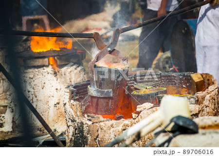 Shot of Thai blacksmith holding a hot crucible by the iron pliers from furnace. Gold melting process with gasoline burner in crucible. Shot of Thai blacksmith holding a hot crucible by the iron pliers from furnace. Gold melting process with gasoline burner in crucible. 89706016