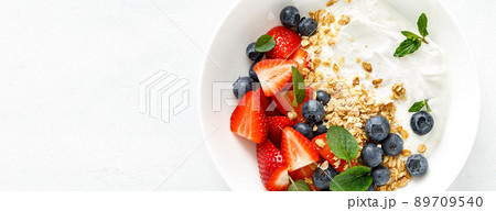 Breakfast bowl with granola, plain yogurt, strawberry and blueberry. Top view. Banner 89709540