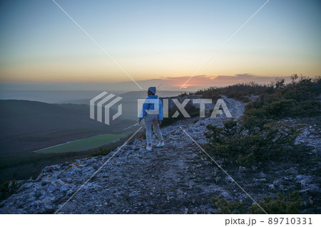 Woman tourist on top of sunrise mountain. The girl salutes the sun, wearing a blue jacket, white hat and white jeans. Conceptual design. Woman tourist on top of sunrise mountain. The girl salutes the sun, wearing a blue jacket, white hat and white jeans. Conceptual design. 89710331