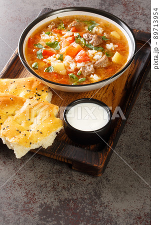 Spicy Uzbek mastava soup with lamb, rice and vegetables close-up in a bowl served with bread and sour milk. vertical 89713954