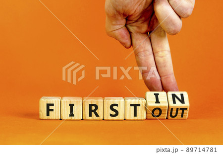 First in first out symbol. Businessman turns wooden cubes and changes words first in to first out. Beautiful orange table, orange background. Business and first in and out concept. Copy space. First in first out symbol. Businessman turns wooden cubes and changes words first in to first out. Beautiful orange table, orange background. Business and first in and out concept. Copy space. 89714781