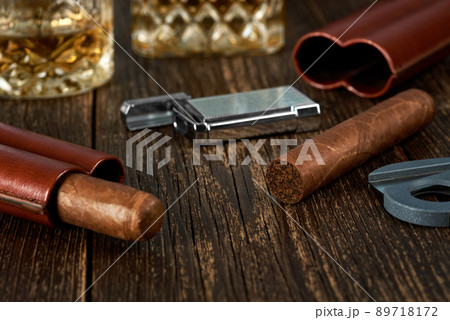 Two Cuban cigars and lighter in a leather case on an old brown table top. 89718172