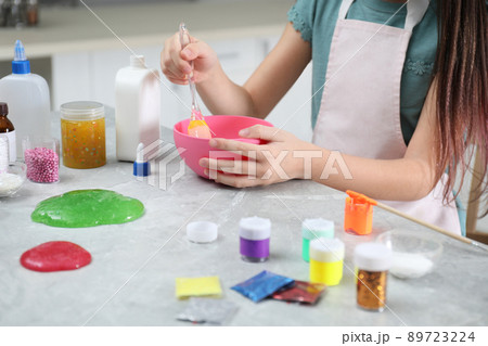Little girl mixing ingredients with silicone spatula at table in kitchen, closeup. DIY slime toy Little girl mixing ingredients with silicone spatula at table in kitchen, closeup. DIY slime toy 89723224