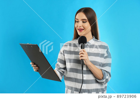 Young female journalist with microphone and clipboard on blue background 89723906
