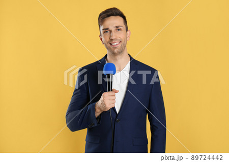 Young male journalist with microphone on yellow background Young male journalist with microphone on yellow background 89724442