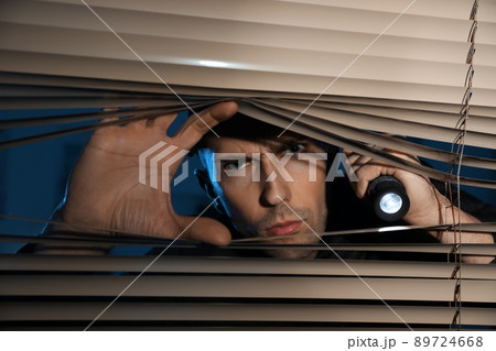Male security guard with flashlight looking through window blinds in darkness 89724668