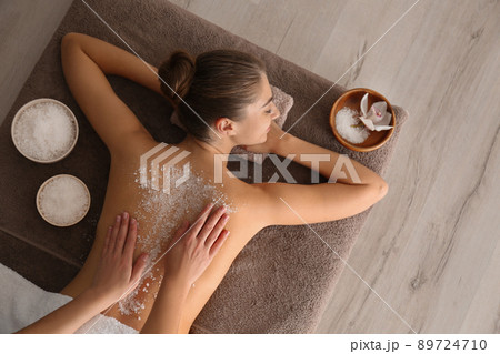 Young woman having body scrubbing procedure with sea salt in spa salon, top view Young woman having body scrubbing procedure with sea salt in spa salon, top view 89724710