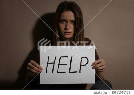 Abused young woman showing palm with word STOP near beige wall, focus on hand 89724712