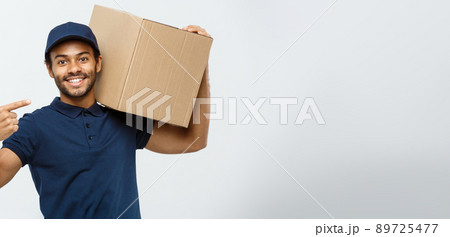 Delivery Concept - Portrait of Happy African American delivery man pointing hand to present a box package. Isolated on Grey studio Background. Copy Space. Delivery Concept - Portrait of Happy African American delivery man pointing hand to present a box package. Isolated on Grey studio Background. Copy Space. 89725477